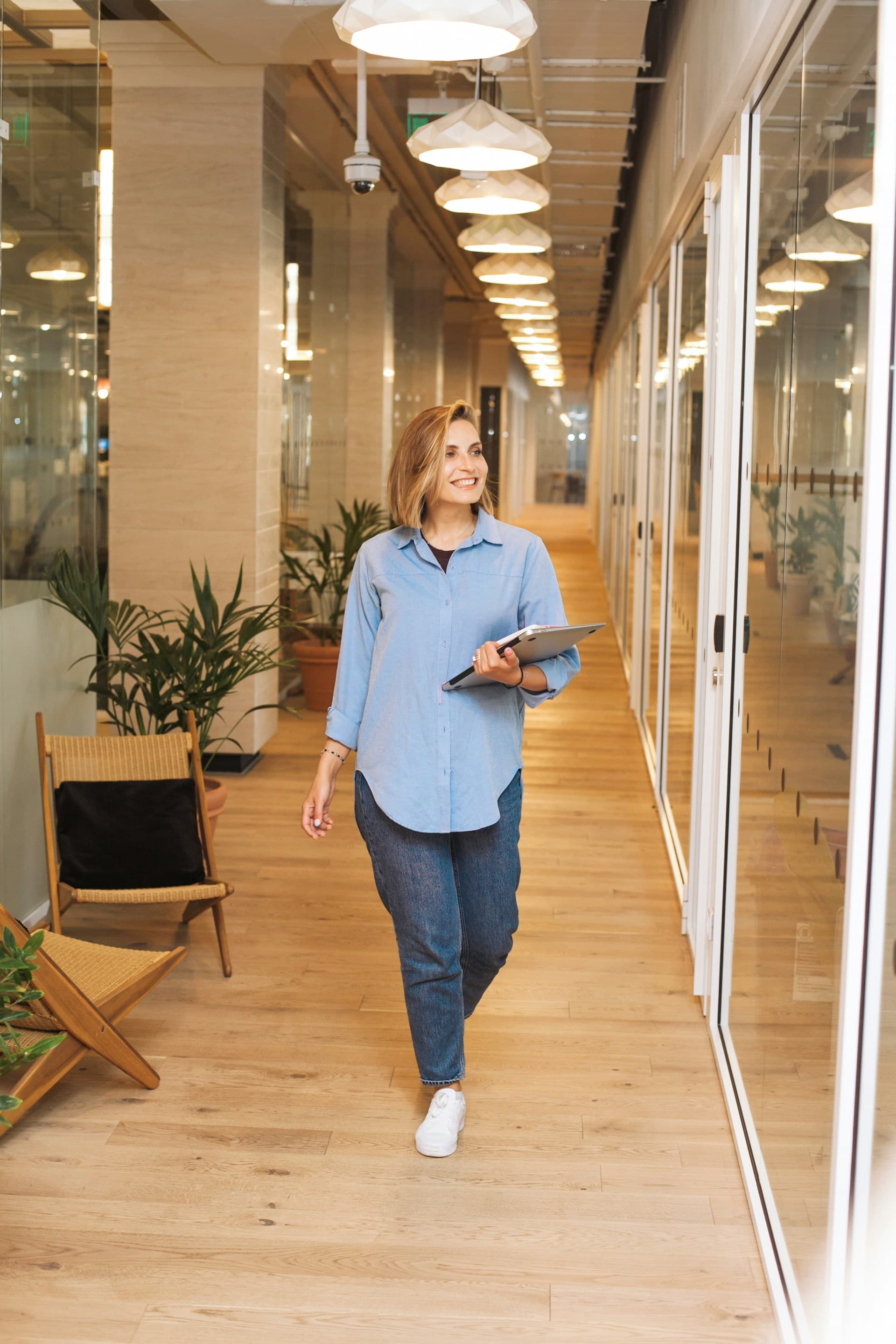 Femme souriant marchant dans un bureau, un ordinateur portable sous le bras